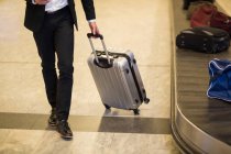 Empresário caminhando com bagagem perto da área de reclamação de bagagem no aeroporto — Fotografia de Stock