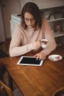 Woman using digital tablet while holding coffee cup at home — Stock Photo