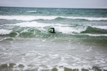 Mann im Neoprenanzug schwimmt im Meer am Strand — Stockfoto