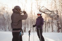 Skier man photographing woman with mobile phone in ski resort — Stock Photo
