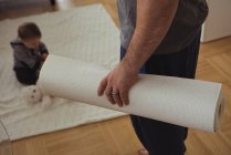 Father holding exercise mat while baby playing in background at home — Stock Photo