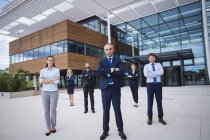 Grupo de empresarios confiados de pie con los brazos cruzados fuera del edificio de oficinas - foto de stock