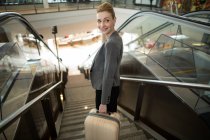 Business woman standing on escalator with luggage at airport — Stock Photo