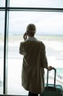 Rückansicht einer Geschäftsfrau mit Gepäck, die am Flughafen mit dem Handy telefoniert — Stockfoto