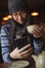 Mulher usando telefone celular enquanto toma café no café — Fotografia de Stock