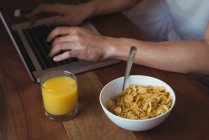 Partie médiane de l'homme utilisant un ordinateur portable tout en prenant le petit déjeuner dans la chambre à coucher à la maison — Photo de stock