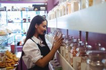 Хозяйка магазина смотрит на банки с турецкими сладостями на полке в магазине — стоковое фото