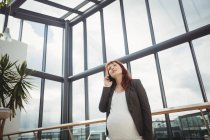 Schwangere Geschäftsfrau telefoniert in Büroflur — Stockfoto