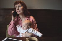 Мать с ребенком разговаривает по мобильному телефону в кафе — стоковое фото