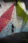Trainer assisting man climbing on artificial wall in gym — Stock Photo