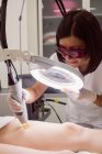 Крупним планом лікар, що виконує лазерну епіляцію на шкірі стегна пацієнта в клініці — стокове фото