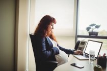 Schwangere Geschäftsfrau berührt Bauch, während sie Laptop im Büro benutzt — Stockfoto