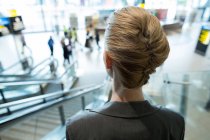 Vista trasera de la mujer de negocios bajando en escaleras mecánicas en la terminal del aeropuerto - foto de stock