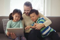 Madre sonriente y niños usando tableta digital en la sala de estar - foto de stock
