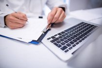 Mid section of doctor writing on clipboard in clinic — Stock Photo