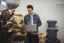 Man using laptop while standing besides coffee grinding machine in coffee shop — Stock Photo