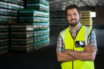 Retrato de un trabajador varón confiado con los brazos cruzados de pie en el almacén - foto de stock