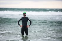 Retrato de atleta em terno molhado em pé com as mãos nos quadris no mar — Fotografia de Stock