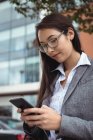 Businesswoman text messaging on mobile phone while standing at city street — Stock Photo