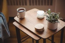 Tasse à thé, sous-verres et plante de maison sur table en bois dans le salon à la maison — Photo de stock