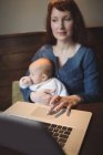 Mother with infant daughter using laptop in cafe — Stock Photo