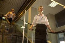 Equipe feminina descendo da escada rolante no terminal do aeroporto — Fotografia de Stock