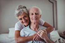 Portrait of senior woman embracing senior man on bed in bed room — Stock Photo