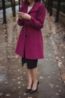 Cropped view of businesswoman using phone standing on autumnal pathway — Stock Photo