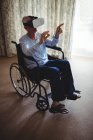 Homme âgé assis sur fauteuil roulant et utilisant casque de réalité virtuelle dans la chambre à coucher à la maison — Photo de stock