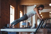 Женщина практикует пилатес на реформаторе в фитнес-студии — стоковое фото