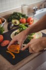 Primo piano delle mani maschili affettare il peperone sul tagliere in cucina — Foto stock