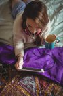 Женщина пользуется цифровым планшетом, когда дома пьет кофе — стоковое фото