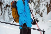 Sección media del esquiador caminando con esquí en montañas cubiertas de nieve - foto de stock