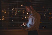 Hombre usando su tableta digital cerca de persianas de ventana en la noche - foto de stock