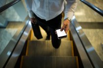 Meio-seção de homem usando telefone celular na escada rolante no aeroporto — Fotografia de Stock