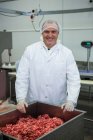 Portrait de boucher debout avec récipient plein de viande hachée dans l'usine de viande — Photo de stock