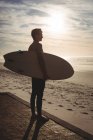 Silueta de surfista masculino de pie con tabla de surf en la playa - foto de stock