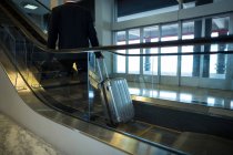 Вид сзади бизнесмена на эскалаторе в аэропорту — стоковое фото