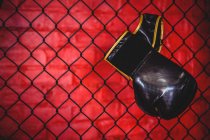 Guante de boxeo colgado en valla de malla de alambre en gimnasio - foto de stock