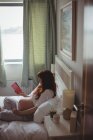 Беременная женщина читает книгу на кровати в спальне — стоковое фото