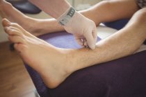 Закри фізіотерапевт, виконуючи сухий пункція на ноги пацієнта в клініку — стокове фото