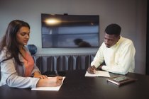 Businesswoman and colleague writing in a diary in conference room at office — Stock Photo