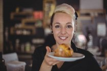 Portrait of waitress holding plate with muffin in cafe — Stock Photo