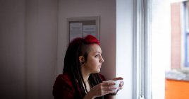 Mulher olhando pela janela enquanto toma café no café — Fotografia de Stock