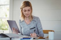 Schöne Frau schreibt Tagebuch, während sie zu Hause ein digitales Tablet benutzt — Stockfoto