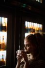 Bella donna che prende il caffè oltre all'esposizione del vino nel bar — Foto stock