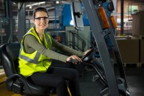 Ritratto di bella lavoratrice che guida carrello elevatore in magazzino — Foto stock