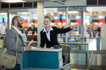 Flugbegleiter zeigt Pendlern am Check-in-Schalter im Flughafenterminal die Richtung — Stockfoto