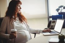 Schwangere Geschäftsfrau benutzt Laptop beim Kaffee im Büro — Stockfoto
