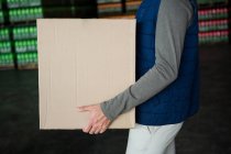 Mid section of worker carrying cardboard box in warehouse — Stock Photo